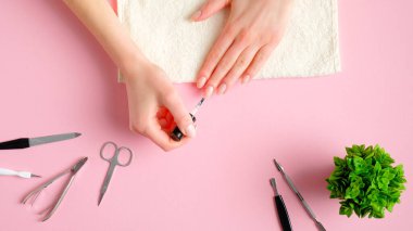 Kadın kendine manikür yapıyor. Tırnak cilası, manikür ve pembe arka planda pedikür aletleri olan kadın elleri, yukarıdan görüş. Kişisel bakım güzellik tedavi konsepti