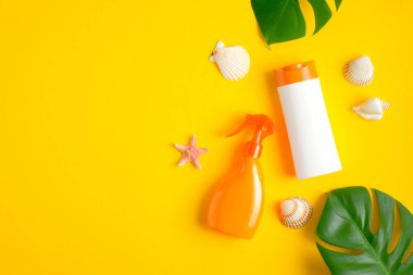 Güneş kremi ve sprey şişeleri tropikal yapraklar ve deniz kabuklarıyla sarı arka planda modellenir. Güneş koruması ve plaj cilt bakımı kavramı