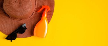 Etiketsiz güneş kremi spreyi, sarı arka planda plaj şapkası ve güneş gözlüğü. Düz yerde, üst tarafta. Yaz güneş kremi kozmetik ürünlü bir blog afişi tasarımı. Güneş koruma kavramı
