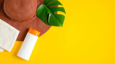 Etiketsiz güneş kremi, plaj şapkası, sarı arka planda tropikal yaprak. Düz yerde, üst tarafta. Yaz cilt bakımı kozmetik ürünleri ile birlikte blog afişi tasarımı. Güneş koruma kavramı