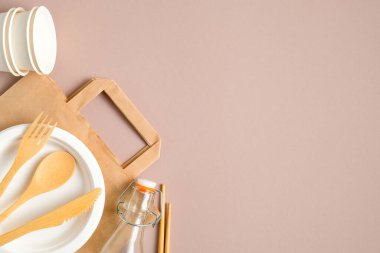 Biyo-çözünebilir kağıt torba, tahta çatal bıçak, cam şişe, kağıt bardak ve bambu pipetli plastik set. Düz yerde, üst tarafta. Sıfır atık, çevre dostu konsept. Sürdürülebilir yaşam tarzı.