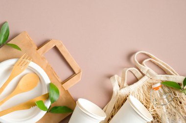 Biyo-çözünebilir kağıt torbalı plastik set, ahşap sofra takımı, geri dönüştürülmüş içme bardakları, cam sicim torbası, yeşil yapraklar. Sıfır atık, çevre dostu konsept. Sürdürülebilir yaşam tarzı. Üst görünüm.