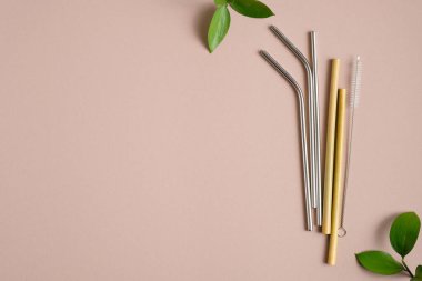 Kahverengi arka planda yeşil yaprakları olan çeşitli çevre dostu pipetler. Düz yerde, üst tarafta. Sıfır atık, plastik ücret konsepti. Sürdürülebilir yaşam tarzı.