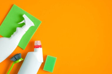 Ev temizliği konsepti. Üst manzara temizlik malzemeleri, temiz şişeler, fırça, turuncu arka planda yeşil hijyenik peçete ve sünger.