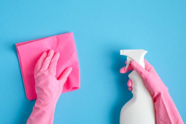 Elinde temizlik spreyi şişesi ve mavi arka planda hijyenik peçete tutan pembe eldivenli kadın elleri. Ev temizliği ya da temizlik konsepti
