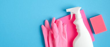 Ev temizliği hizmeti konsepti. Mavi arka planda temizlik malzemeleri. Üst manzara pembe sünger, lastik eldiven, peçete ve temizlik spreyi şişesi.