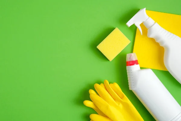 Cleaning equipment set on green background. Top view yellow sponge, rubber gloves, cleaner bottles. Cleaning services concept.