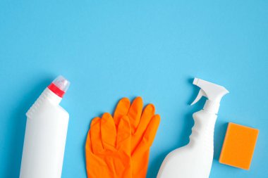 Mavi arka planda ev temizleme malzemeleri. Temizlik hizmeti ve temizlik konsepti. Lastik sprey şişesi, temizlik deterjanı, turuncu sünger ve lastik eldiven..