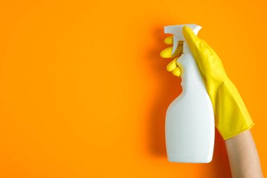 Sarı kauçuk eldiven içinde plastik sprey tutarken turuncu bir arka planda temizlik deterjanı vardı.