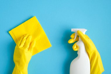 Temizlik hizmeti konsepti. Sarı eldivenli, mavi arka planda bez ve temizleyici sprey şişeli eller.