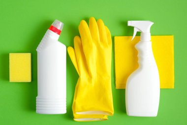 Yeşil arka planda temizlik malzemeleri var. Düz sarı bez ve sünger, lastik eldivenler, daha temiz sprey şişesi, deterjan. Ev temizliği ve temizlik konsepti.