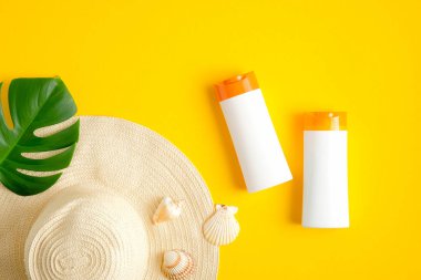 Güneş kremi şişeleri, tropikal yapraklar ve sarı arka planda bayan plaj şapkası. Yaz güneşi kozmetik ürünleri konseptini koruyor. Düz yatış, üst görünüm