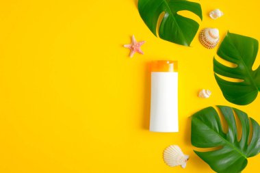 Güneş kremi kremi şişesi maketi ve sarı arka planda tropik yapraklar. Yaz güneşi kozmetik ürün konseptini koruyor. Düz yatış, üst görünüm