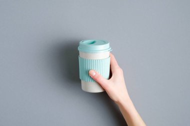 Gri arkaplanı kadın eli ile yeniden kullanılabilir kahve kupası. Çevre dostu bambu kupası, sıfır atık konsepti