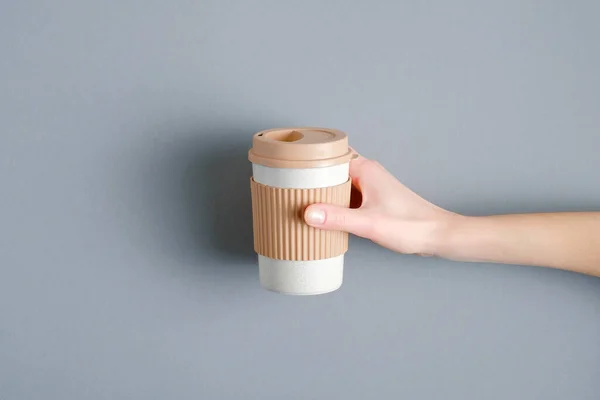 Reusable coffee cup in female hand over grey background. Eco friendly bamboo mug, zero waste concept