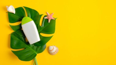 Güneş kremi şişesi ve sarı arka planda tropikal yapraklar. Yaz tatili kavramında güneş koruması