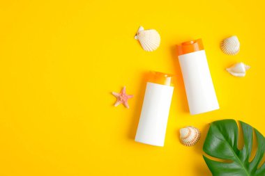 Sarı arka planda iki beyaz plastik güneş kremi şişesi, deniz kabuğu ve tropikal yaprak. Güneş koruması, güneş kremi kozmetik ürünleri, yaz cilt bakımı konsepti. Düz yatıyordu, üst