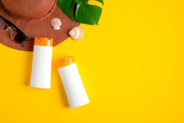 Beyaz plastik şişelerde güneş kremi, plaj şapkası ve sarı arka planda tropikal yaprak. Güneş kremi, güneş kremi kozmetik ürünü, yaz cilt bakımı konsepti. Düz yatış, üst görünüm