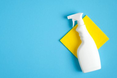 Beyaz, boş, deterjanlı sprey sprey şişesi ve mavi arka planda sarı bez. Ev temizliği ve oda servisi konsepti. Düz yatış, üst görünüm.