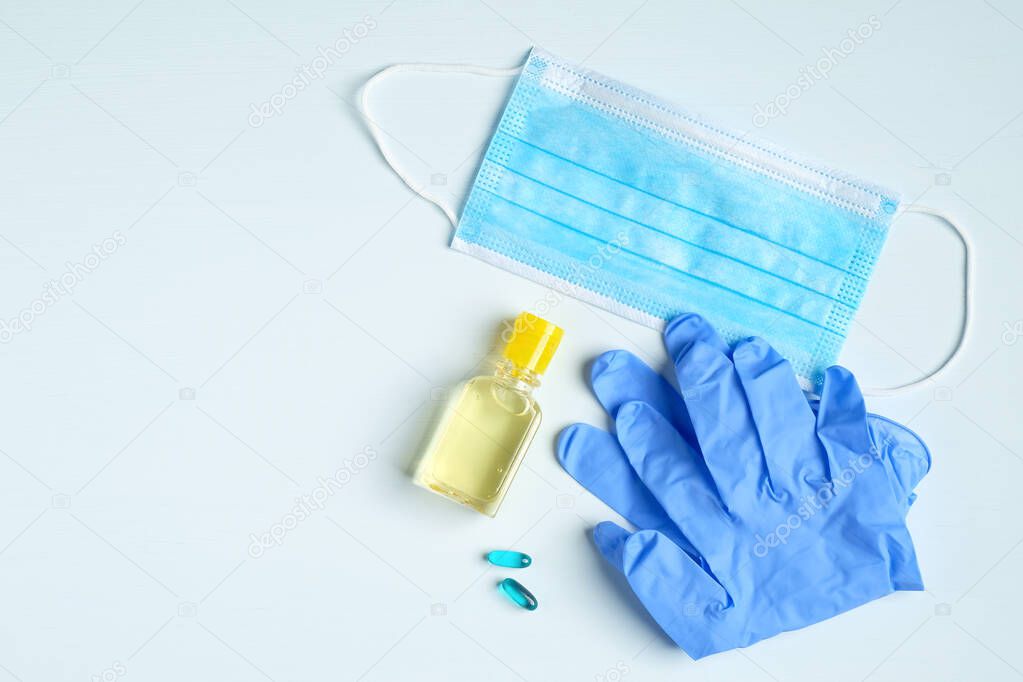 Hand sanitizer gel bottle, face mask, rubber gloves, pills on blue background. Coronavirus Disease (Covid-19) prevention and health protection during flu virus outbreak concept.