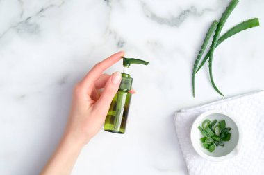 Aloe vera jel yeşil plastik şişe kadın eli mermer arka planda aloe saplı. El ve yüz bakımı için doğal organik losyon. Üst manzara, düz uzanma
