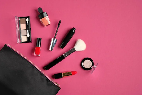 Makeup bag with cosmetic products spilling out on to pink background. Flat lay, view from above. Elegant make up artist pouch with beauty products