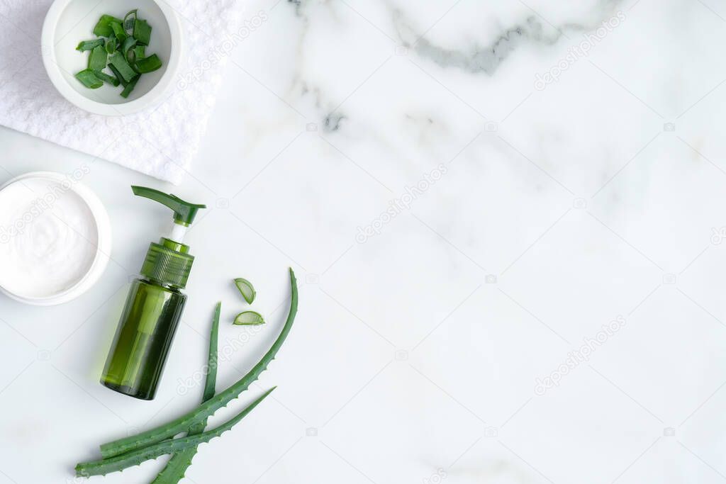 Aloe vera spa treatment concept. Top view green bottle with aloe vera gel, hand cream and sliced stems aloe vera on marble background. Organic natural skincare products
