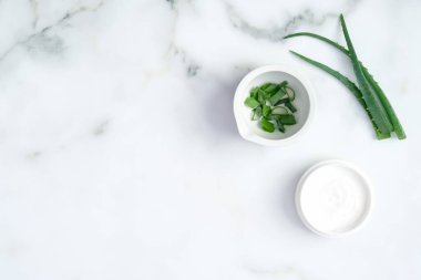 Organik nemlendirici el kremi kavanozu ve mermer zemin üzerinde dilimlenmiş aloe vera kökü. Düz yerde, üst tarafta. El bakımı ve güzellik tedavi konsepti.