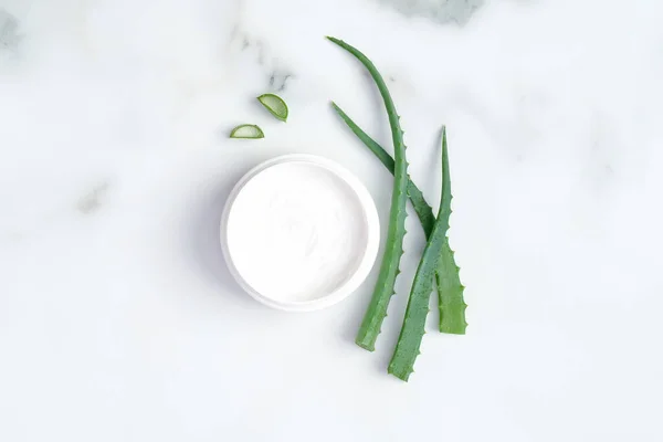 Organik kozmetik cilt nemlendirici krem kavanozu ve mermer zemin üzerinde dilimlenmiş aloe vera kökü. Düz yerde, üst tarafta. Cilt bakımı ve güzellik tedavi kavramı.