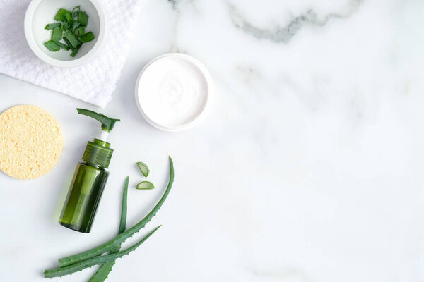 Natural organic SPA cosmetic lotion bottle, sponge and sliced stems aloe vera on marble background. Flat lay, top view. Skin care and beauty treatment concept.