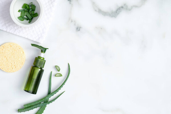 Top view aloe vera gel and sliced plant leaves on marble background. Natural organic SPA cosmetic product. Skincare, cosmetology, dermatology concept.