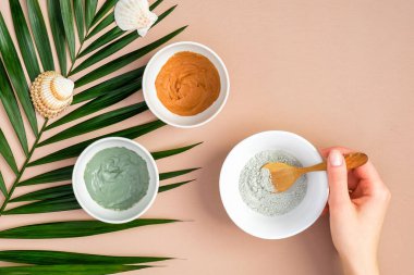 SPA yüz maskelerini ev konseptine göre hazırlamak. Şeftali rengi arka planda, tropik palmiye yaprağıyla ev yapımı yüz kilinden maskeler. Üst manzara, düz uzanma.