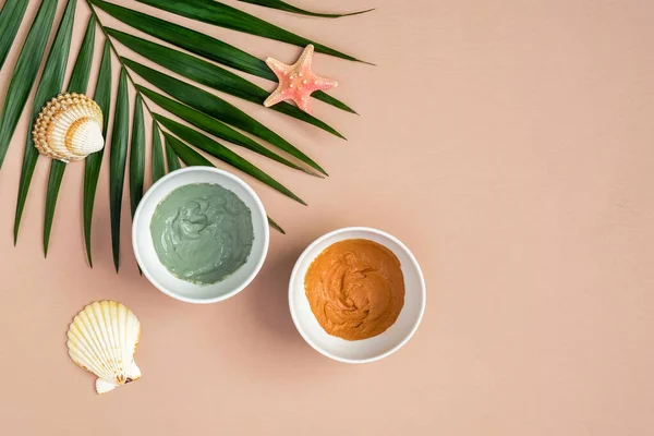 Homemade clay masks in bowls and tropical palm leaf on peach background. Natural organic SPA cosmetic product, face skin care, beauty treatment concept. Flat lay, top view.