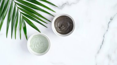 Kaselerde SPA yüz killi maskeleri ve mermer arka planda tropikal yapraklar. Düz yerde, üst tarafta. Doğal organik güzellik ürünleri, yüz bakımı konsepti.