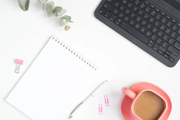 スタイリッシュなオフィステーブルデスク ノートパソコン 紙のノートパッド ピンクのコーヒーカップと白い背景にクリップを持つ女性のワークスペース フラットレイアウト トップビュー — ストック写真