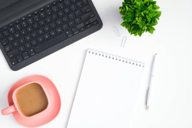 Diz üstü bilgisayarı, kağıt not defteri ve beyaz arka planda kahve fincanı olan şık bir kadınsı çalışma alanı. Modern ofis masası. Düz yatış, üst görünüm