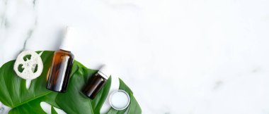 Gerekli yağ şişeleri, lif süngeri ve mermer zemin üzerinde dev tropik bitki yaprakları olan nemlendirici krem. Düz konum, üst görünüm, kopyalama alanı. Cilt bakımı ve güzellik tedavi kavramı