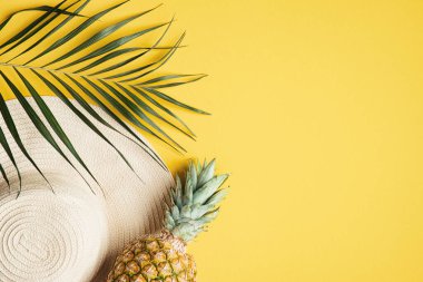 Üst görünüm palmiye yaprağı, kadın plaj şapkası, sarı arka planda ananas ve metin için boşluk. Seyahat ya da tatil konsepti. Gezgin aksesuarlarıyla yaz arkaplanı