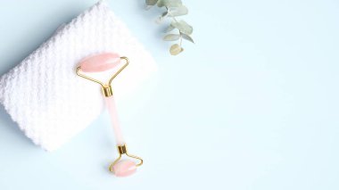 Mavi arka planda okaliptüs yaprağı ve havlu ile gül kuvars yüz masajı silindiri. Yeşim taşlı yüz masajı aleti, yaşlanmayı önleyici, kırışıklık önleyici, cilt bakımı aleti.