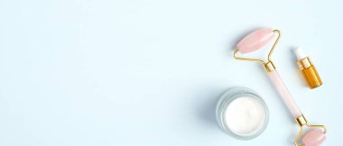 Gül kuvars yüz masajı silindiri, nemlendirici yüz kremi ve mavi arka planda gerekli yağ. Yüz masajı aleti, yaşlanma karşıtı, kırışıklık önleyici güzellik konsepti
