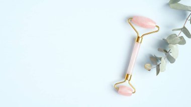 Mavi arka planda okaliptüs yaprağı olan gül kuvars yüz silindiri. Yeşim yüz masajı, yaşlanmayı önleyici, kırışıklık önleyici güzellik aleti.