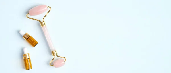 Rose quartz jade stone facial roller and essential oil bottle on blue background. Anti-aging, anti-wrinkle beauty skincare tool