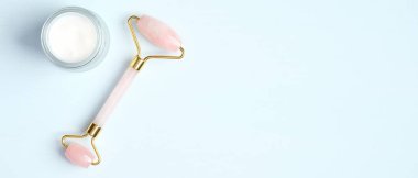 Mavi arka planda nemlendirici krem kavanozlu yüz masajı için gül kuvars silindiri. Düz konum, üst görünüm, kopyalama alanı. Yeşim yüz masajı, cilt bakımı konsepti için güzellik aracı