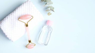 Havlu ve mavi arka planda gerekli yağlı gül kuvars yüz silindiri. Düz konum, üst görünüm, kopyalama alanı. Yeşim yüz masajı aracı, cilt bakımı konsepti için güzellik aracı