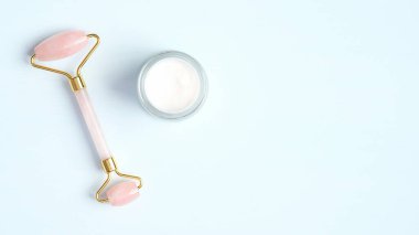 Mavi arka planda nemlendirici krem kavanozlu güzellik masajı için gül kuvars yüz silindiri. Düz konum, üst görünüm, kopyalama alanı