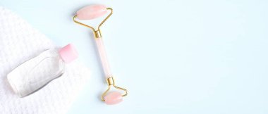 Yeşim, yüz masajı terapisi için gerekli yağ şişesi ve mavi arka planda havlu ile yüz silindiri. Düz konum, üst görünüm, kopyalama alanı