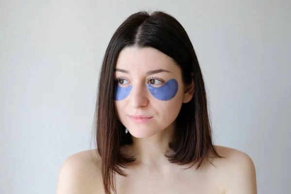 Portrait of beautiful girl with under eye patches. Young woman applying collagen eye mask for puffy. Face skin care and beauty treatment concept.