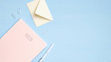 Düz, modern ofis masası. Pembe defterli, zarflı, kalemli, mavi arka planda kırtasiyeli minimum öğrenci çalışma alanı. Eğitim kavramı