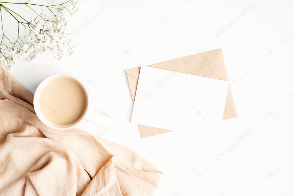 Romantic letter and blank paper card, morning coffee cup, blanket, flower on white wooden background. Cozy home, hygge, comfort concept. Flat lay, top view