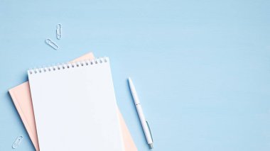 Mavi arka planda not defteri ve kalem. En az kadınsı çalışma alanı, iş ve eğitim konsepti. Düz konum, üst görünüm, kopyalama alanı